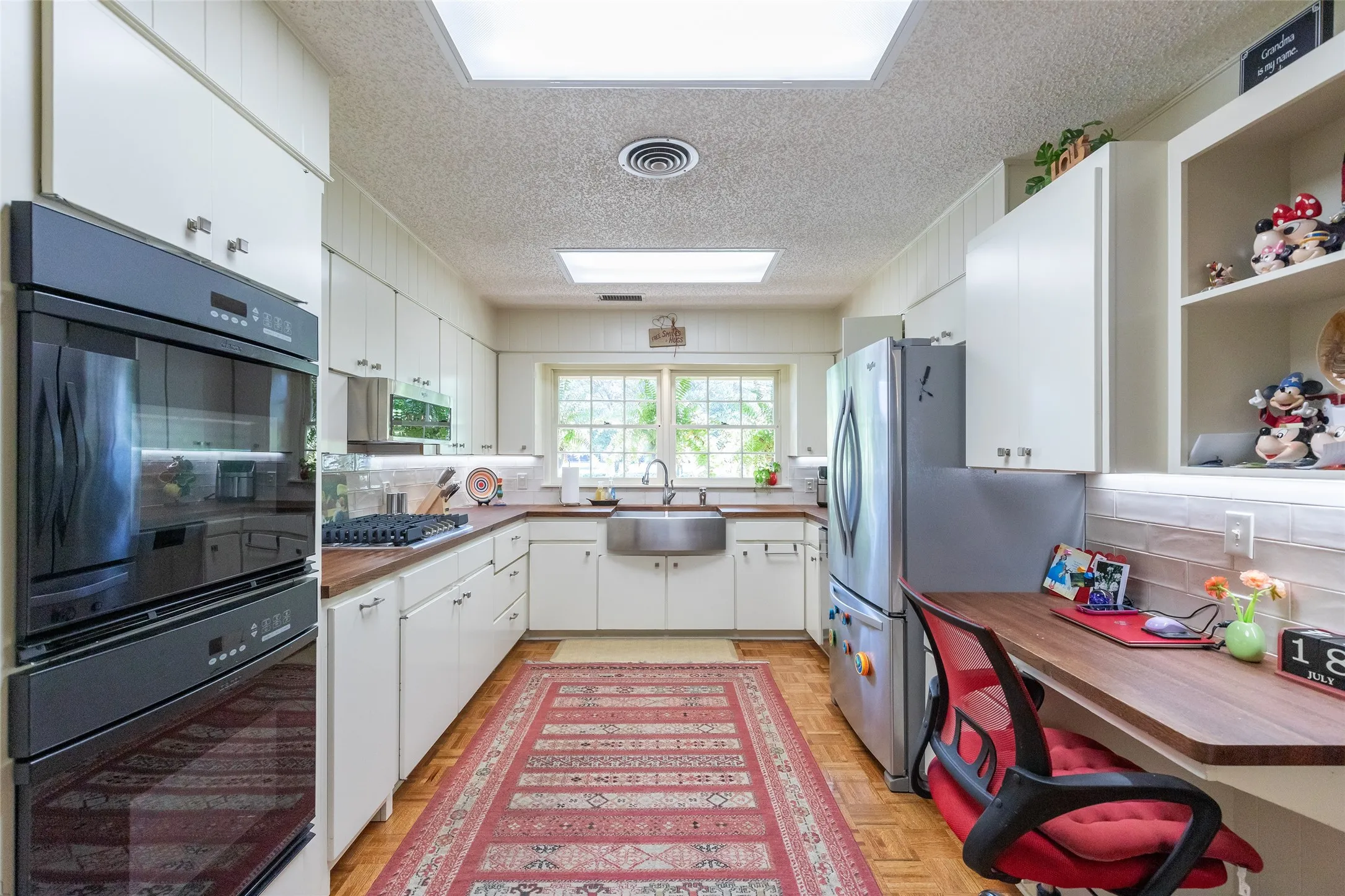 Galley kitchen featuring white cabinetry, wood-finish countertops, stainless steel appliances, a built-in desk, and wood-finish flooring