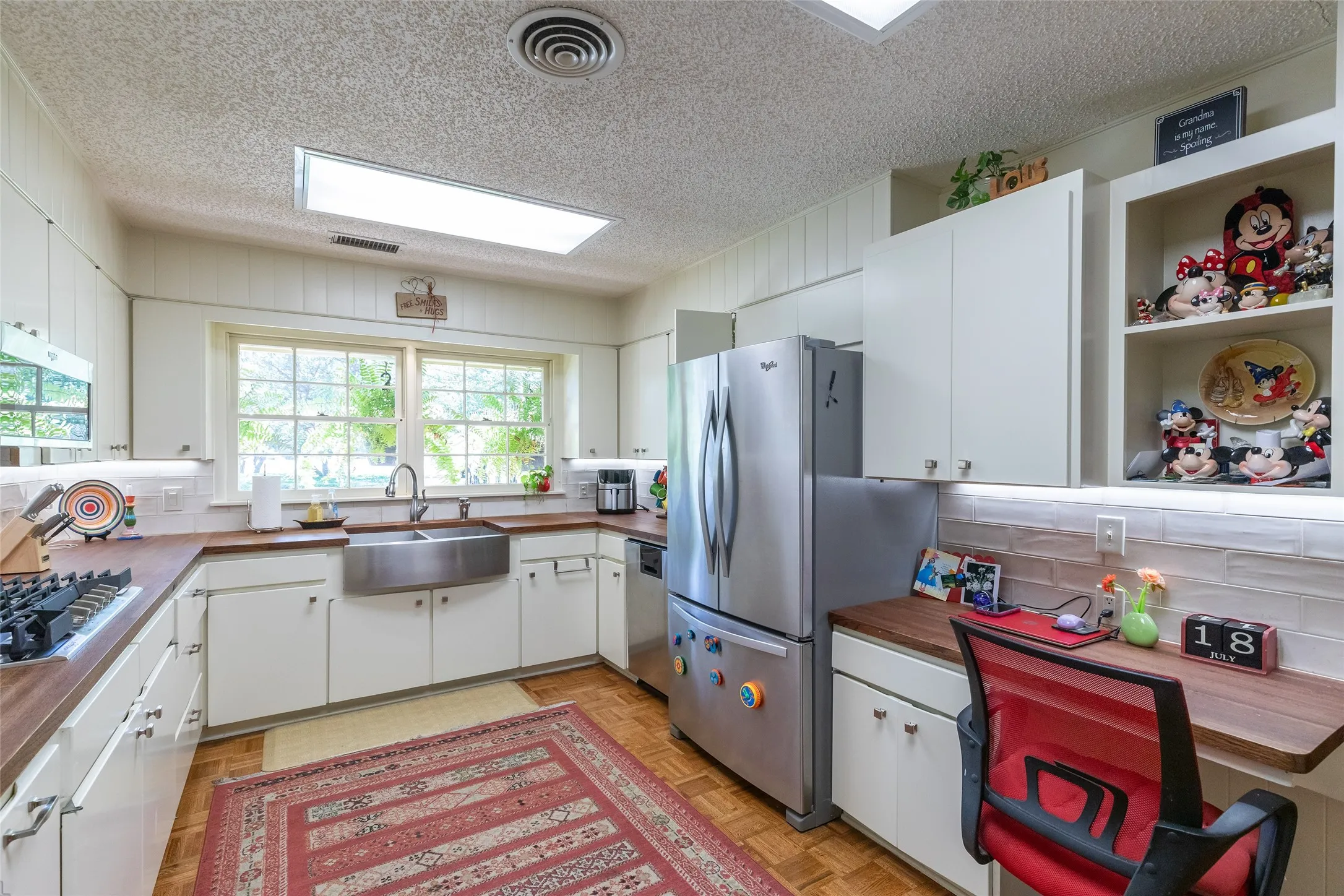 Stainless steel farmhouse sink, white cabinetry with integrated shelving, wood-finish countertops, and a built-in desk area