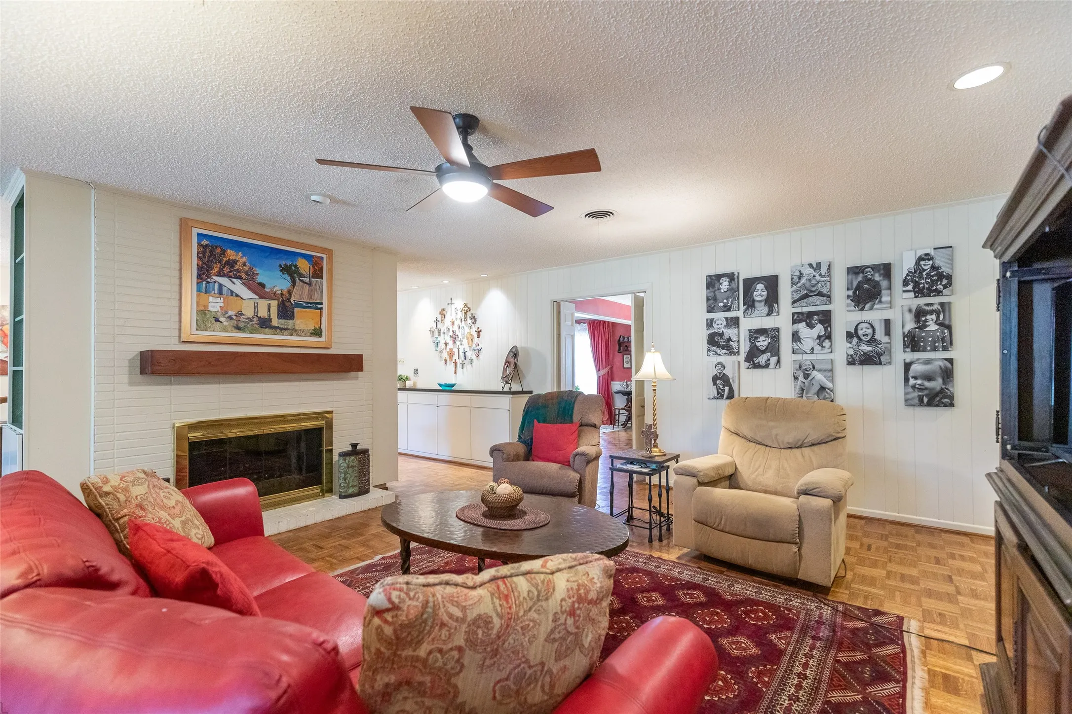 Hardwood parquet flooring, brick fireplace with brass trim, wood mantel, ceiling fan with integrated lighting, and recessed lighting