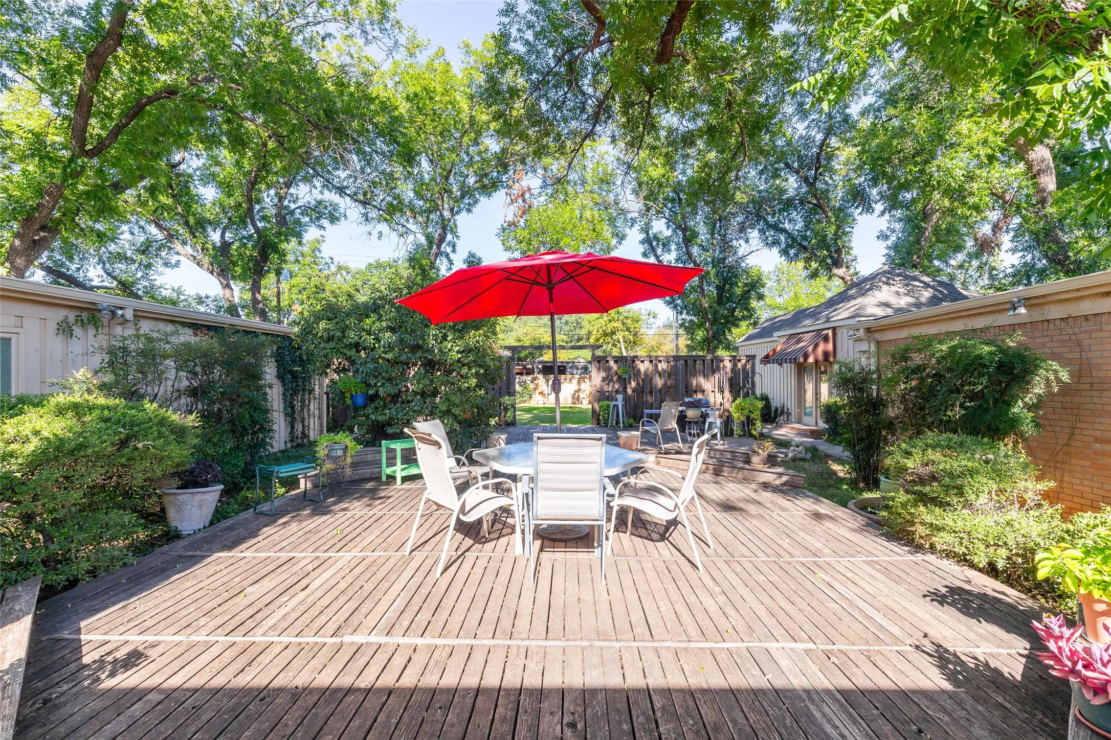 Expansive wood deck with mature perimeter landscaping and partial brick wall detailing