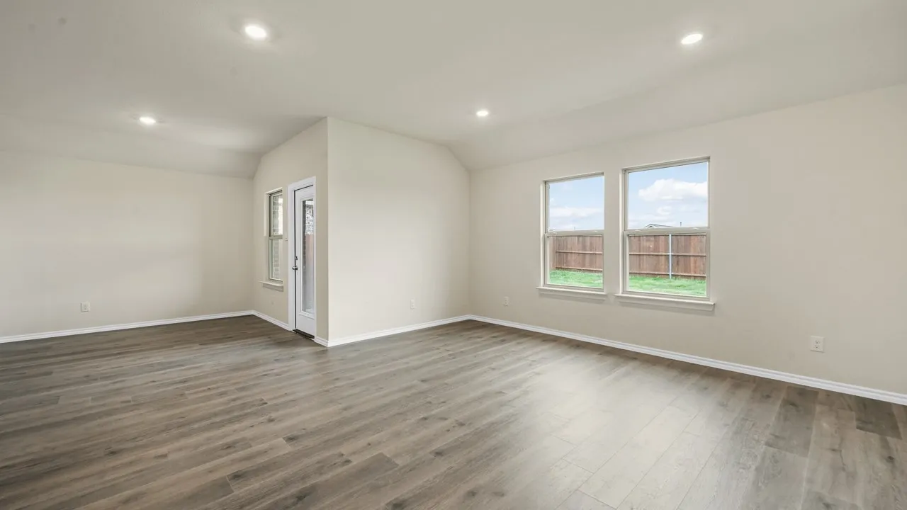 Spacious room featuring wood-finish flooring, recessed lighting, multiple windows, and a glass-paneled door