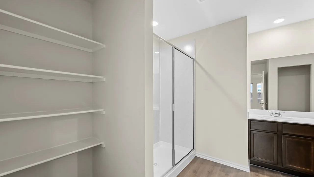 Spacious built-in shelving, glass-enclosed shower, dark wood-finish vanity with countertop, integrated sink, and wood-finish flooring