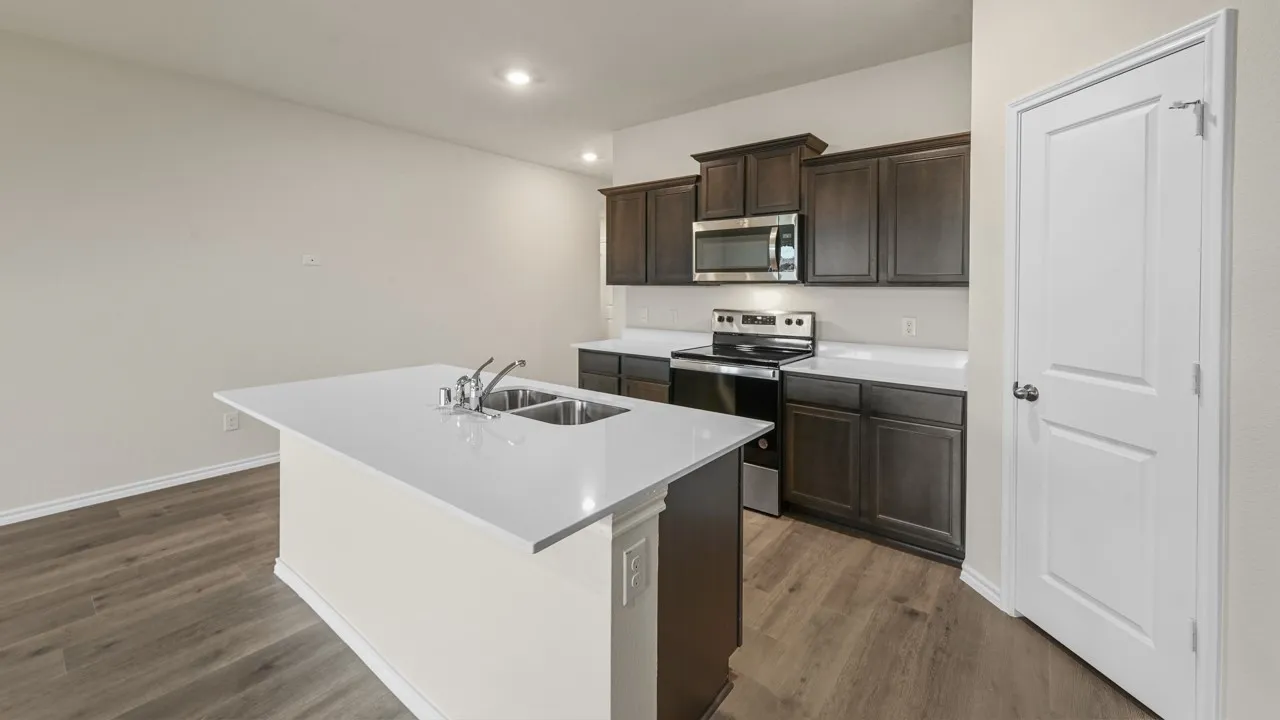 Kitchen featuring dark wood-finish cabinetry, white countertops, stainless steel appliances, and a central island with a double basin sink