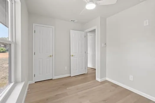 Light wood-finish flooring with crisp white baseboards, a white ceiling fan, and multiple interior paneled doors