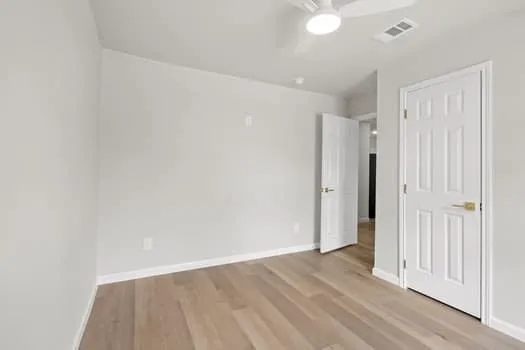 Light wood-finish flooring, white walls, and a ceiling fan with integrated lighting
