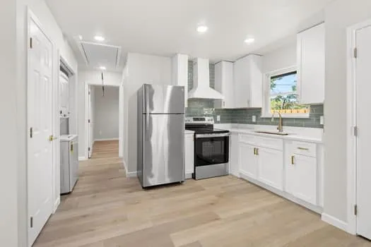 Kitchen featuring stainless steel appliances, white cabinetry, light wood-finish flooring, and a tiled backsplash