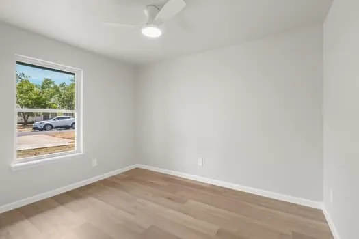 Bright room with wood-finish flooring, white walls, and a ceiling fan with integrated lighting