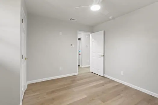 Wood-finish flooring, ceiling fan with integrated lighting, white interior doors, and neutral wall tones