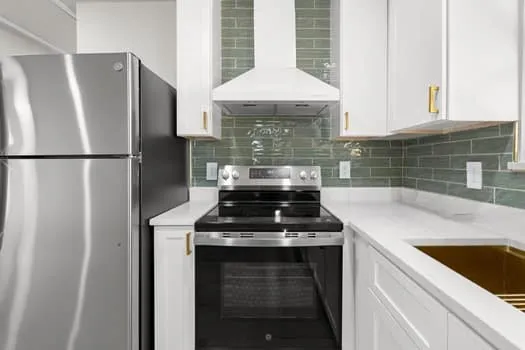Stainless steel appliances, white cabinetry with gold-tone hardware, white countertops, and a green subway tile backsplash