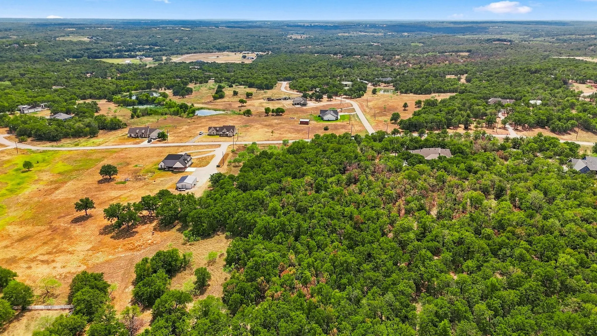 Expansive land with a mix of wooded and open areas, featuring scattered residential properties and natural ponds