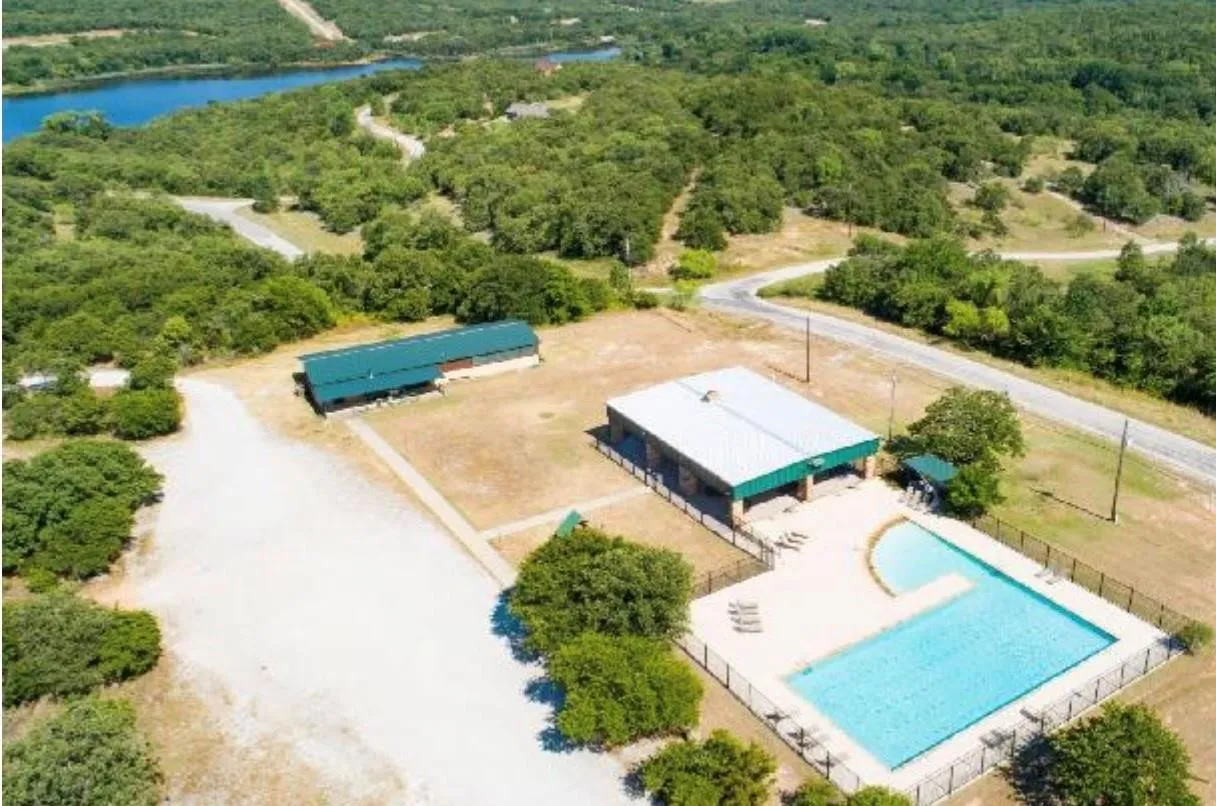 Private community swimming pool with integrated sun ledge, surrounded by a secure metal fence and adjacent to a covered pavilion & Fitness center.