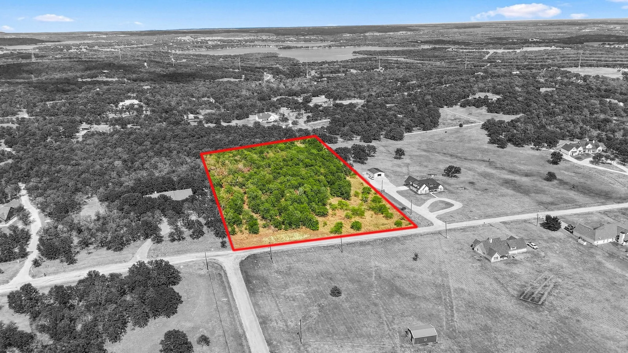 Expansive land parcel featuring a tree-covered area, open fields, and direct road frontage. 310' W X 702' D