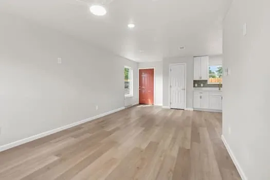 Expansive living area featuring light wood-finish flooring, recessed lighting, and a white paneled door