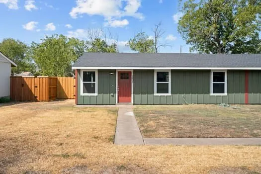 Green vertical siding with red accent, red entry door, white trim windows, dark gray roof, and a wooden privacy fence