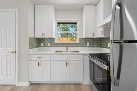 White shaker cabinetry with gold-finish hardware, stainless steel appliances, and a tiled backsplash
