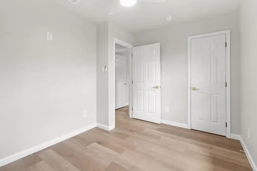 Wood-finish flooring, white walls, white doors with gold-finish hardware, and a ceiling fan