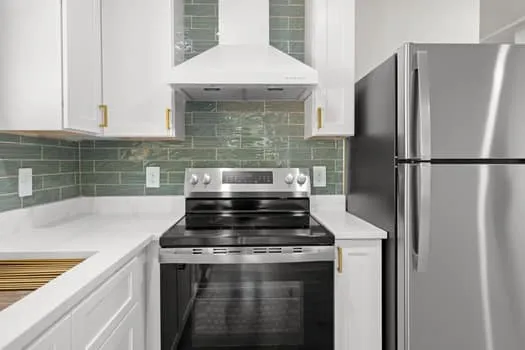 Stainless steel appliances, white cabinetry with gold-tone hardware, white countertops, and a green tile backsplash