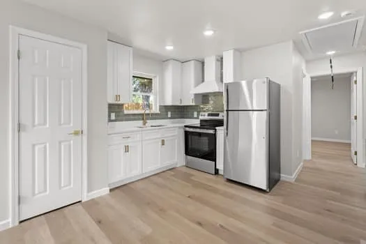 Modern kitchen featuring white cabinetry, light wood-finish flooring, stainless steel appliances, a tile backsplash, and recessed lighting