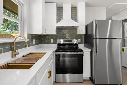 White cabinetry, stainless steel appliances, quartz countertops, a gold-tone faucet, and a subway tile backsplash