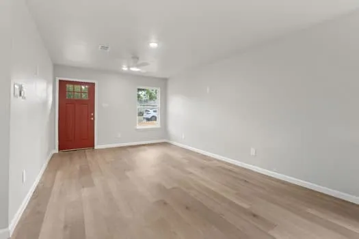 Red paneled entry door with glass inserts, wood-finish flooring, and white ceiling fan