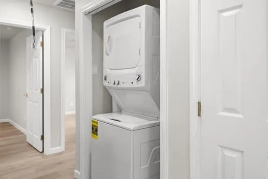 Stackable washer and dryer unit, light wood-finish flooring, white paneled doors, and light gray wall paint