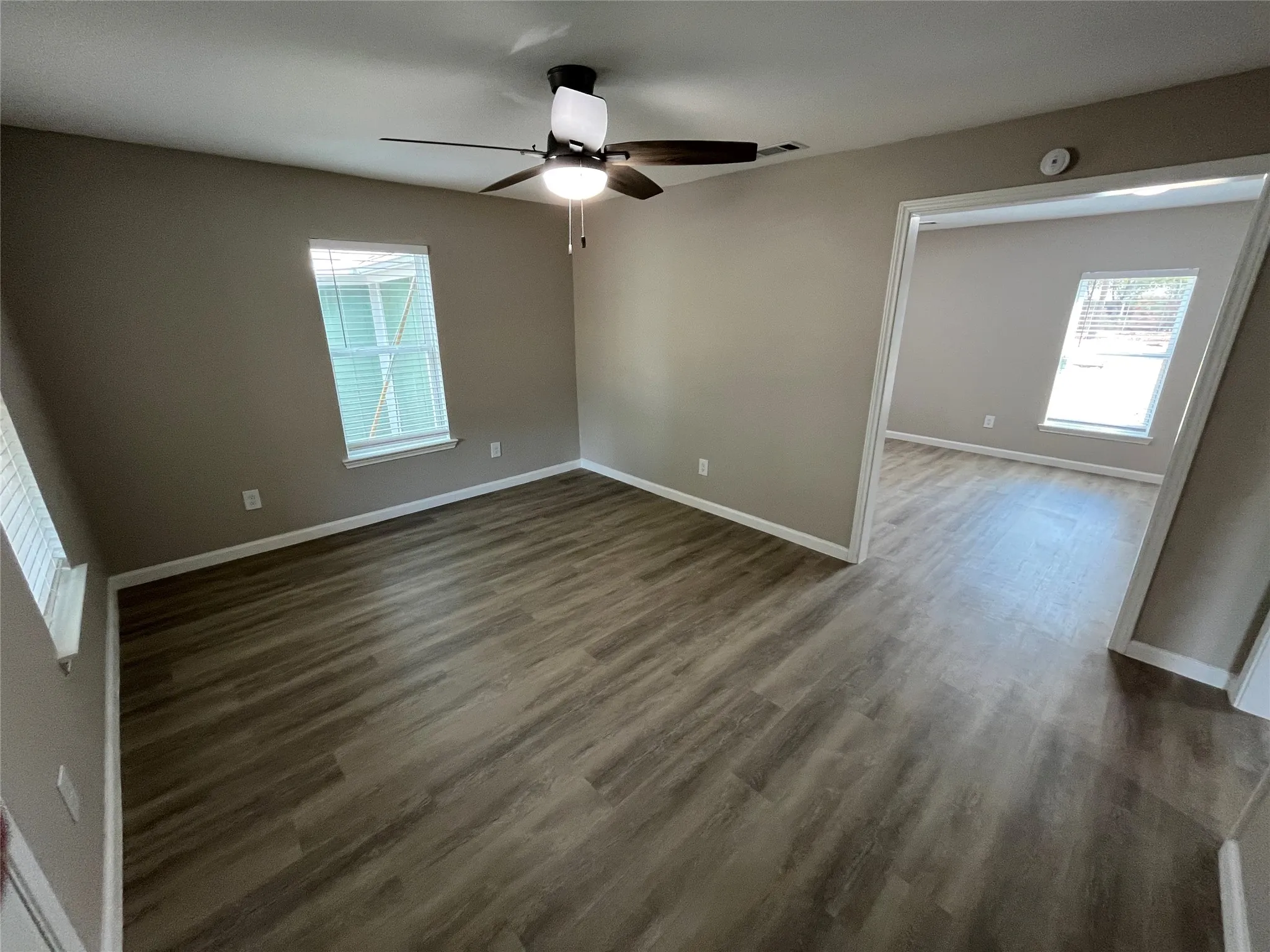Expansive room with wood-finish flooring, neutral wall paint, and a ceiling fan with integrated lighting