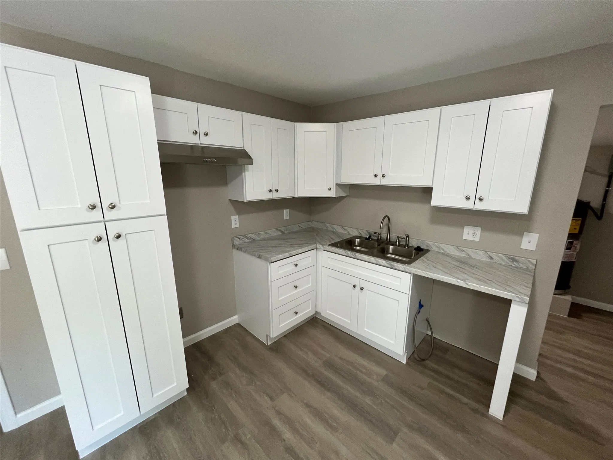 White shaker cabinetry, stainless steel double basin sink, light-toned wood-finish flooring, and light-toned countertops