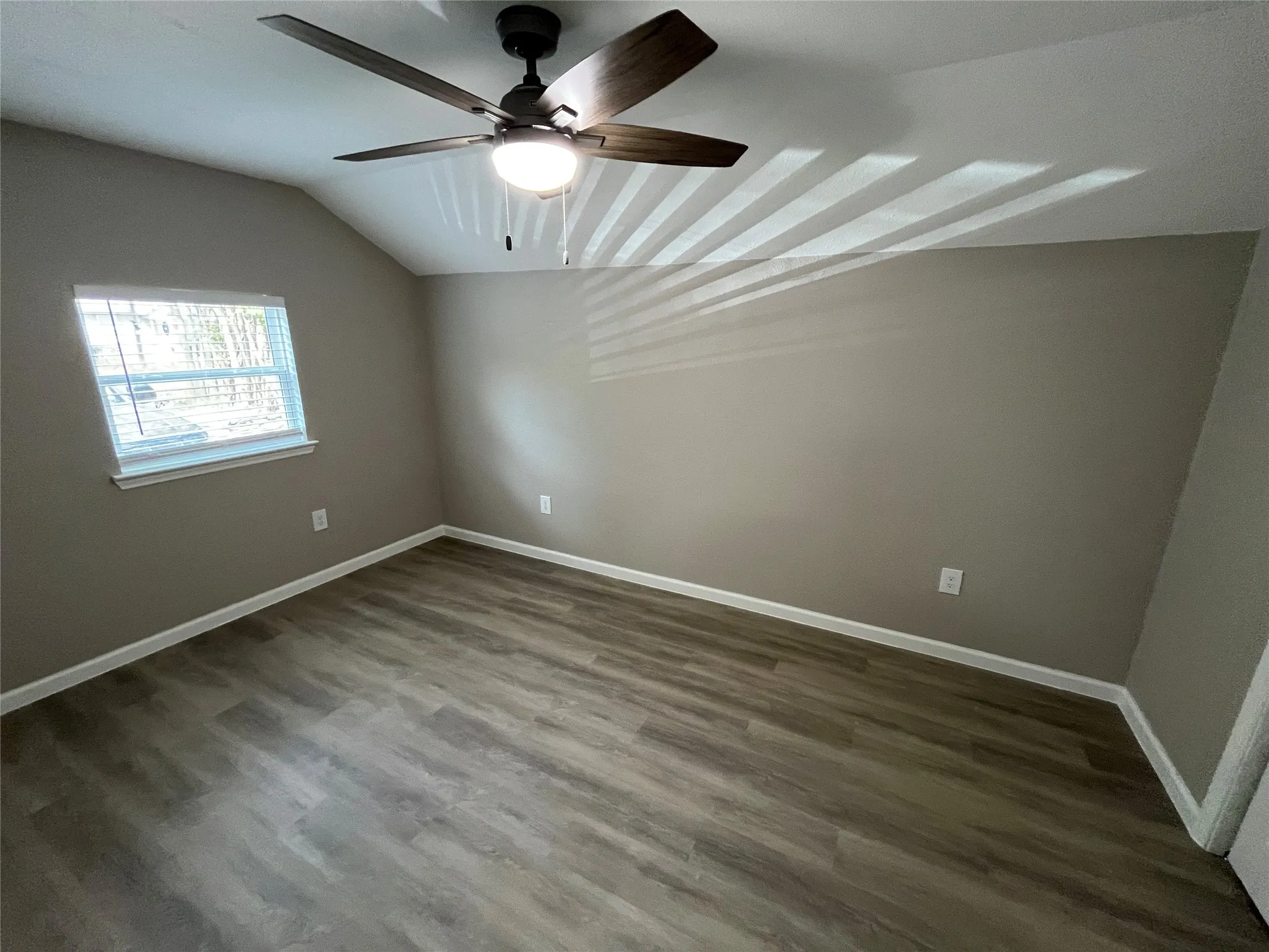 Vaulted ceiling with a ceiling fan and light fixture, wood-finish flooring, and white trim