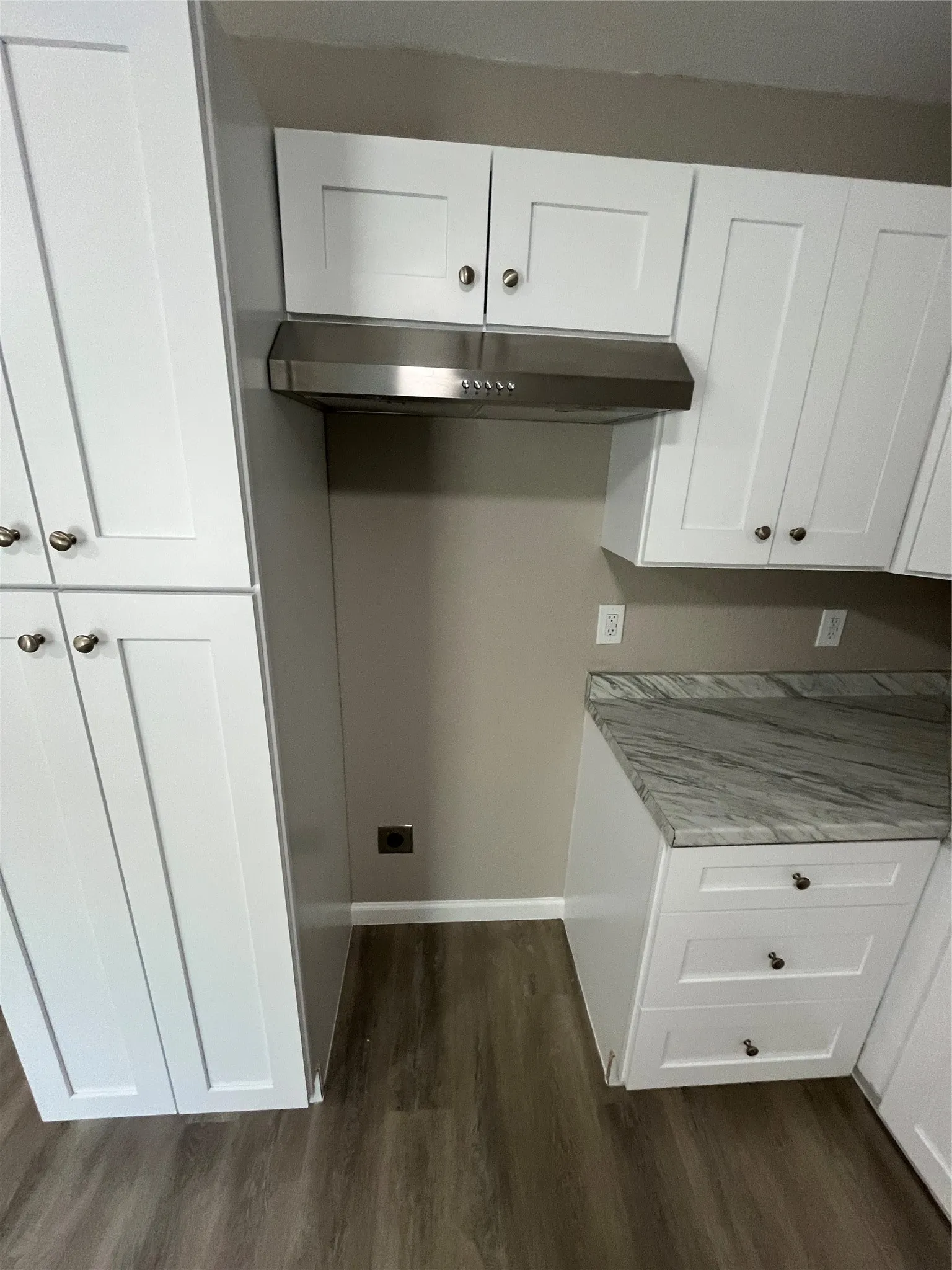 White shaker cabinetry, stainless steel range hood, wood-finish flooring, and gray patterned countertop