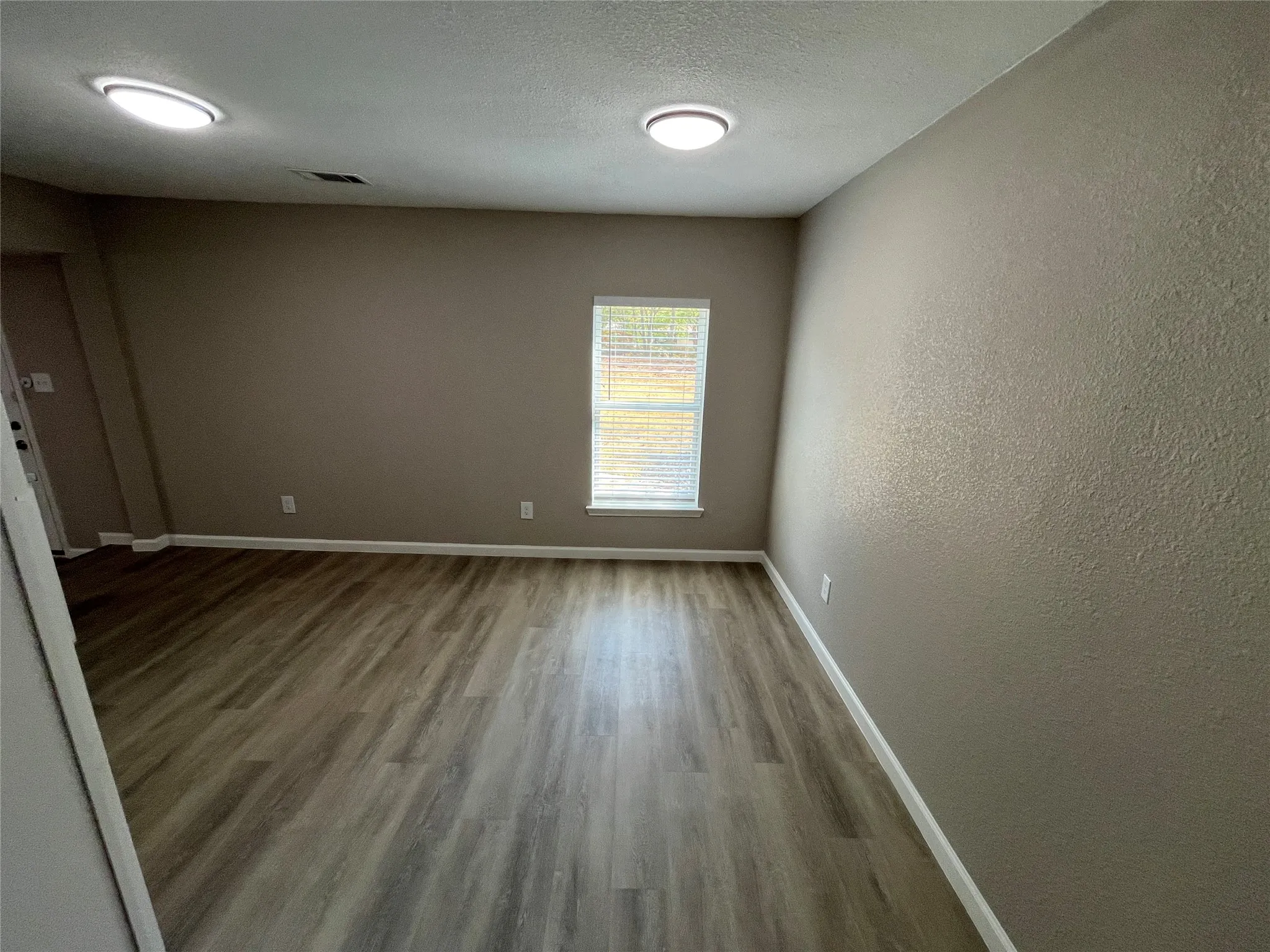 Wood-finish flooring with neutral wall paint, recessed lighting, and a window with blinds