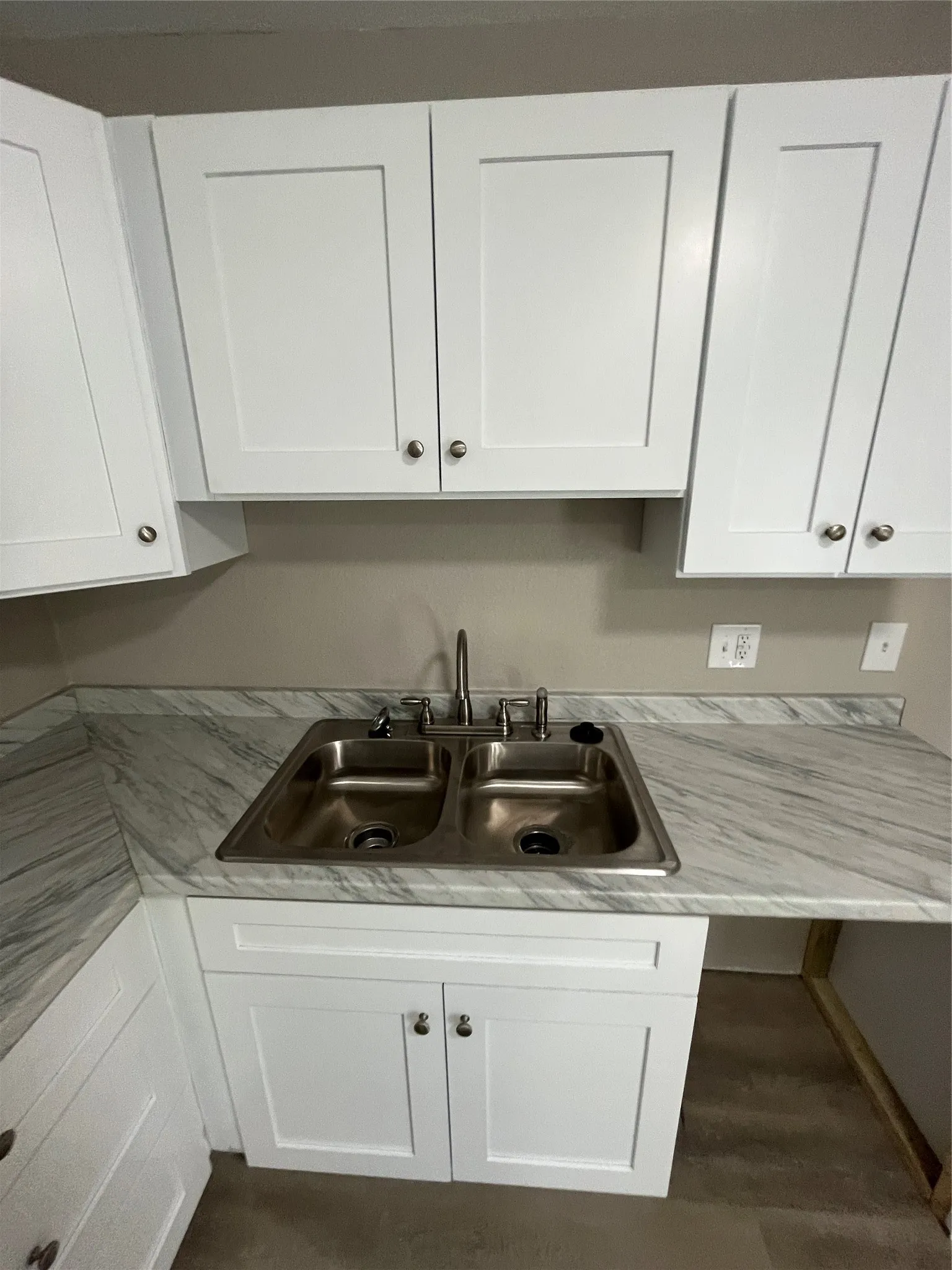 White shaker-style cabinetry with satin nickel hardware, dual basin stainless steel sink with a single-lever faucet, and light-toned, veined countertops