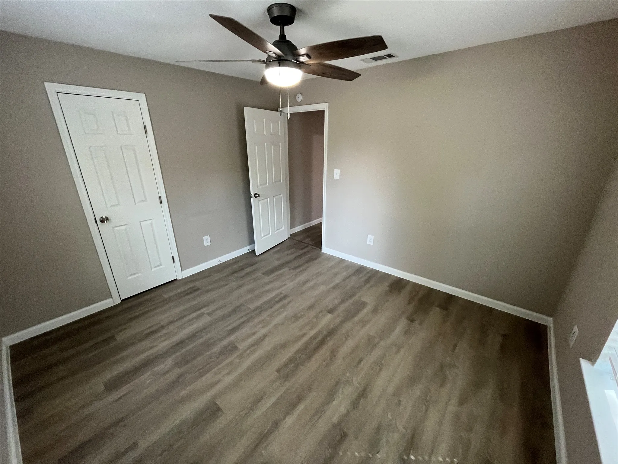 Wood-finish flooring, neutral wall tones, ceiling fan with integrated lighting, and white paneled doors