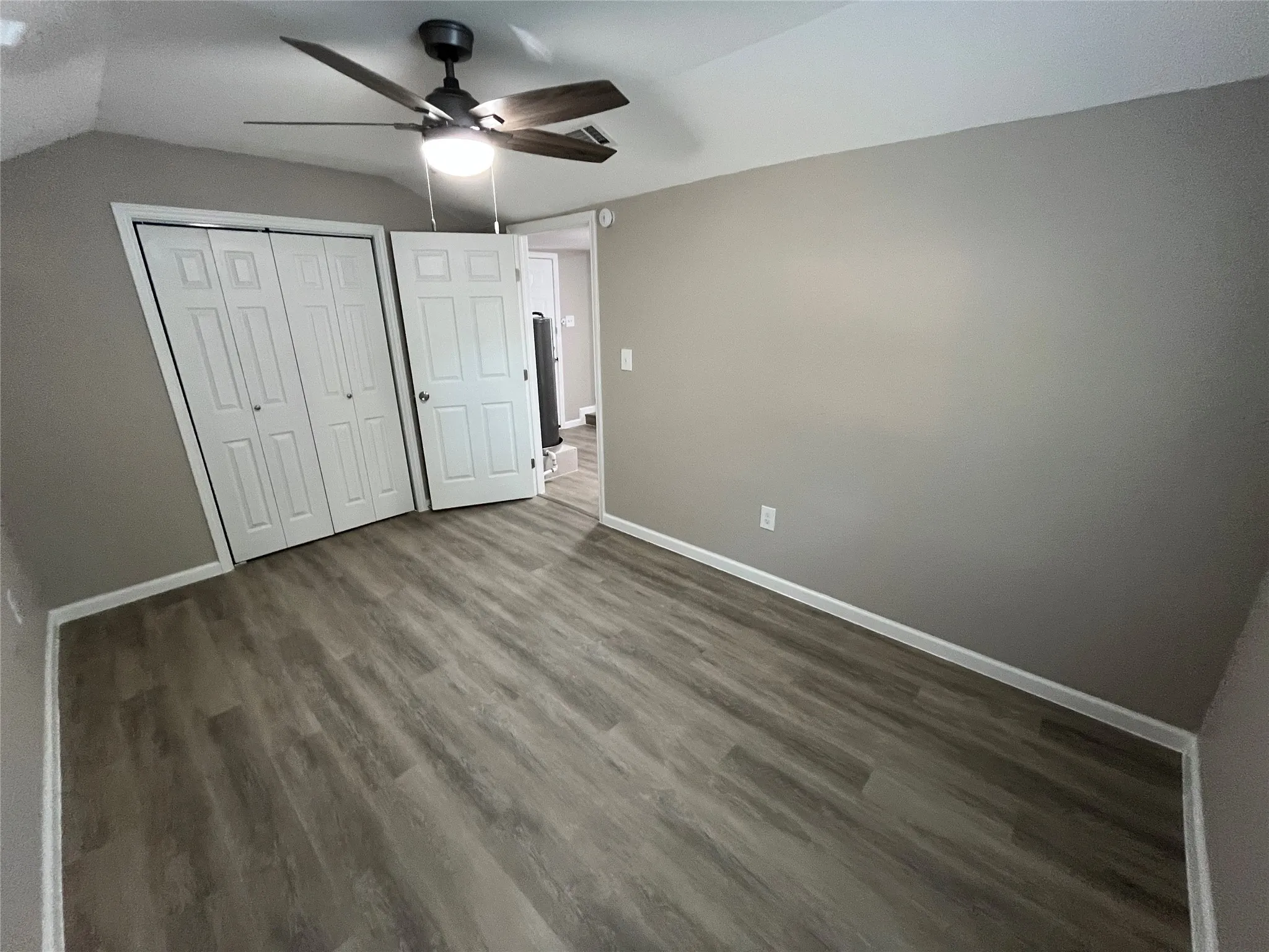 Wood-finish flooring, two bi-fold closet doors, ceiling fan with integrated lighting, and neutral wall tones