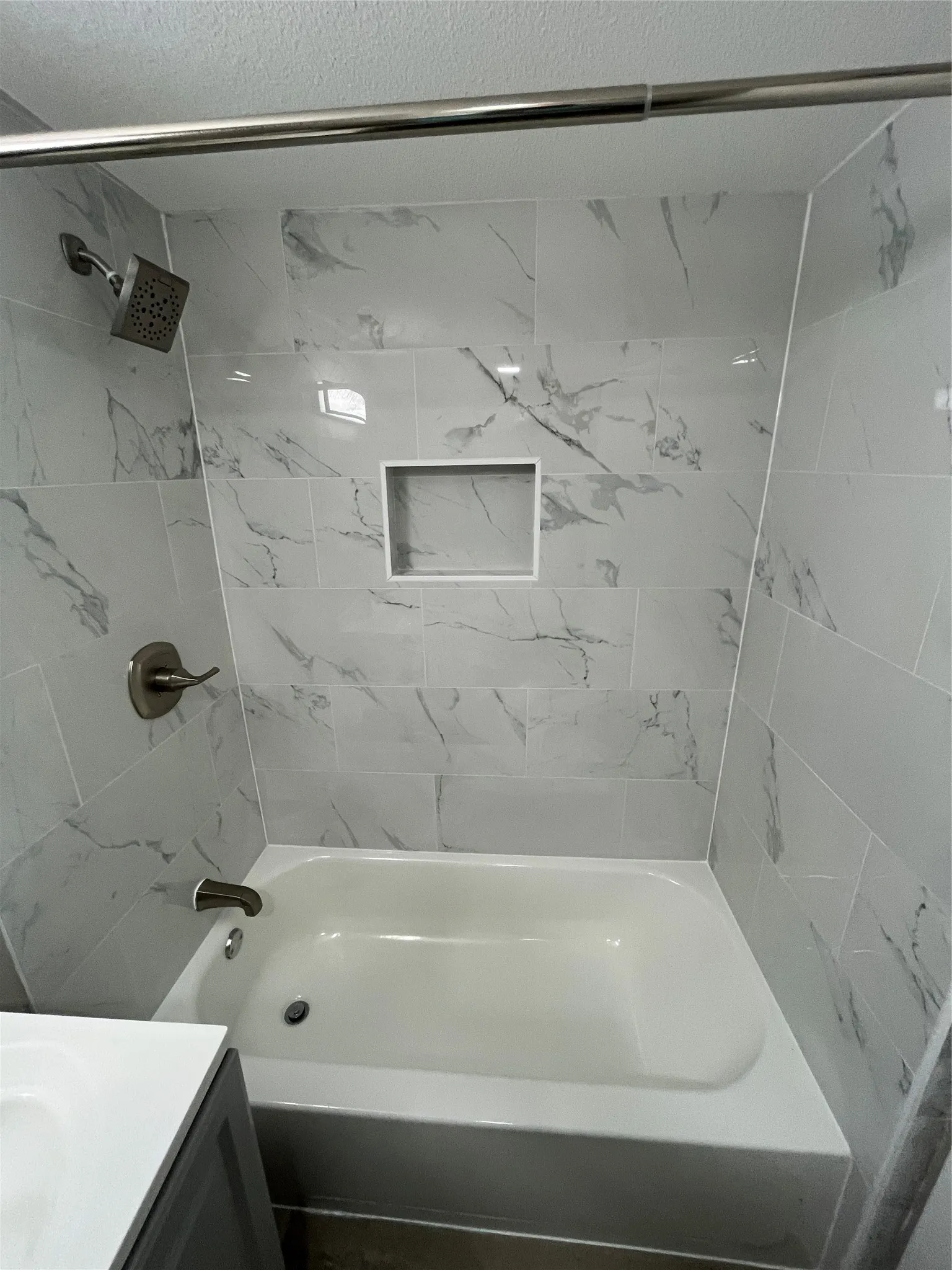 Bathtub with a tiled surround featuring a shower niche, and brushed nickel fixtures
