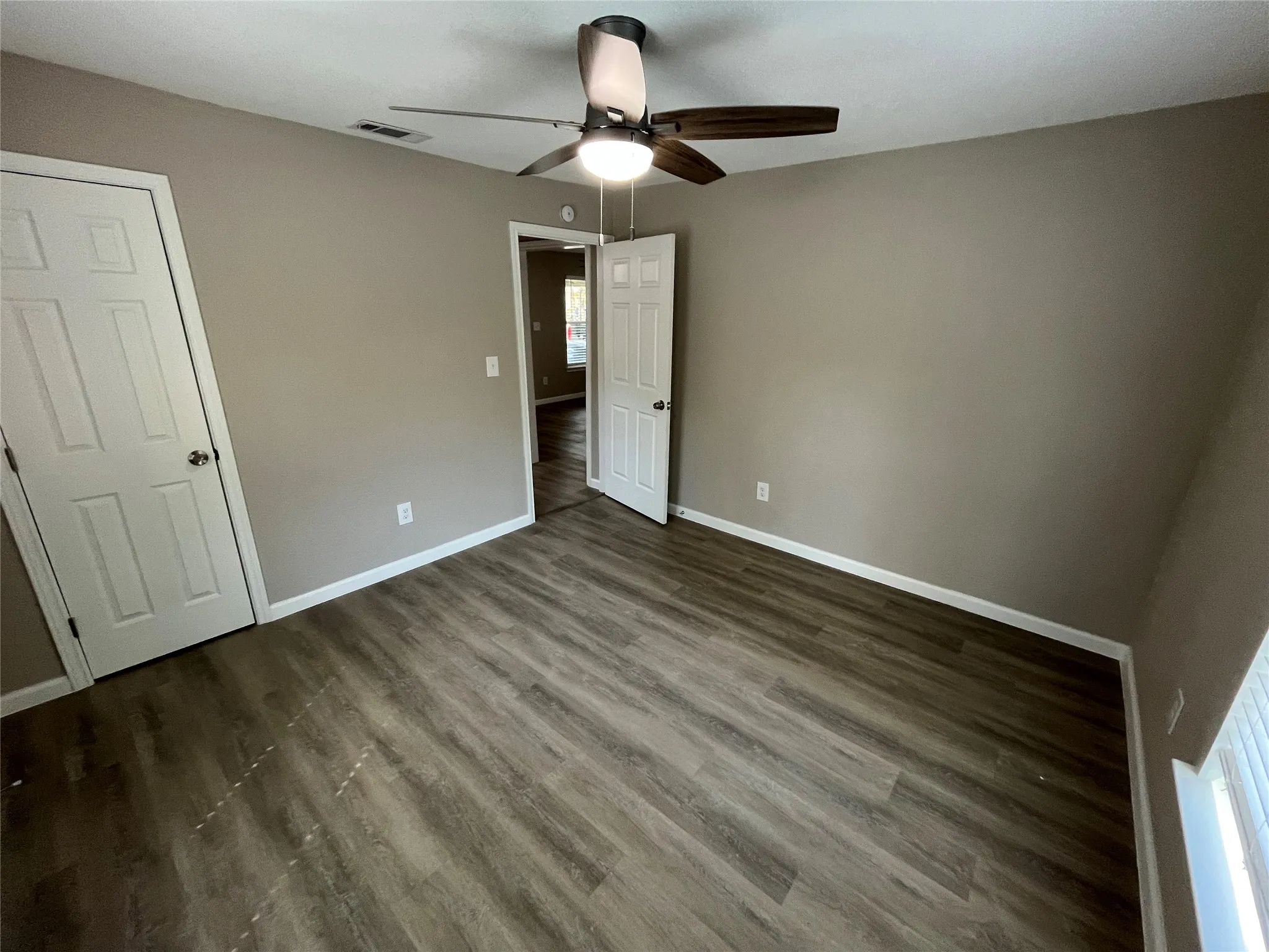 Wood-finish flooring, neutral wall tones, ceiling fan with integrated lighting, and white trim accents