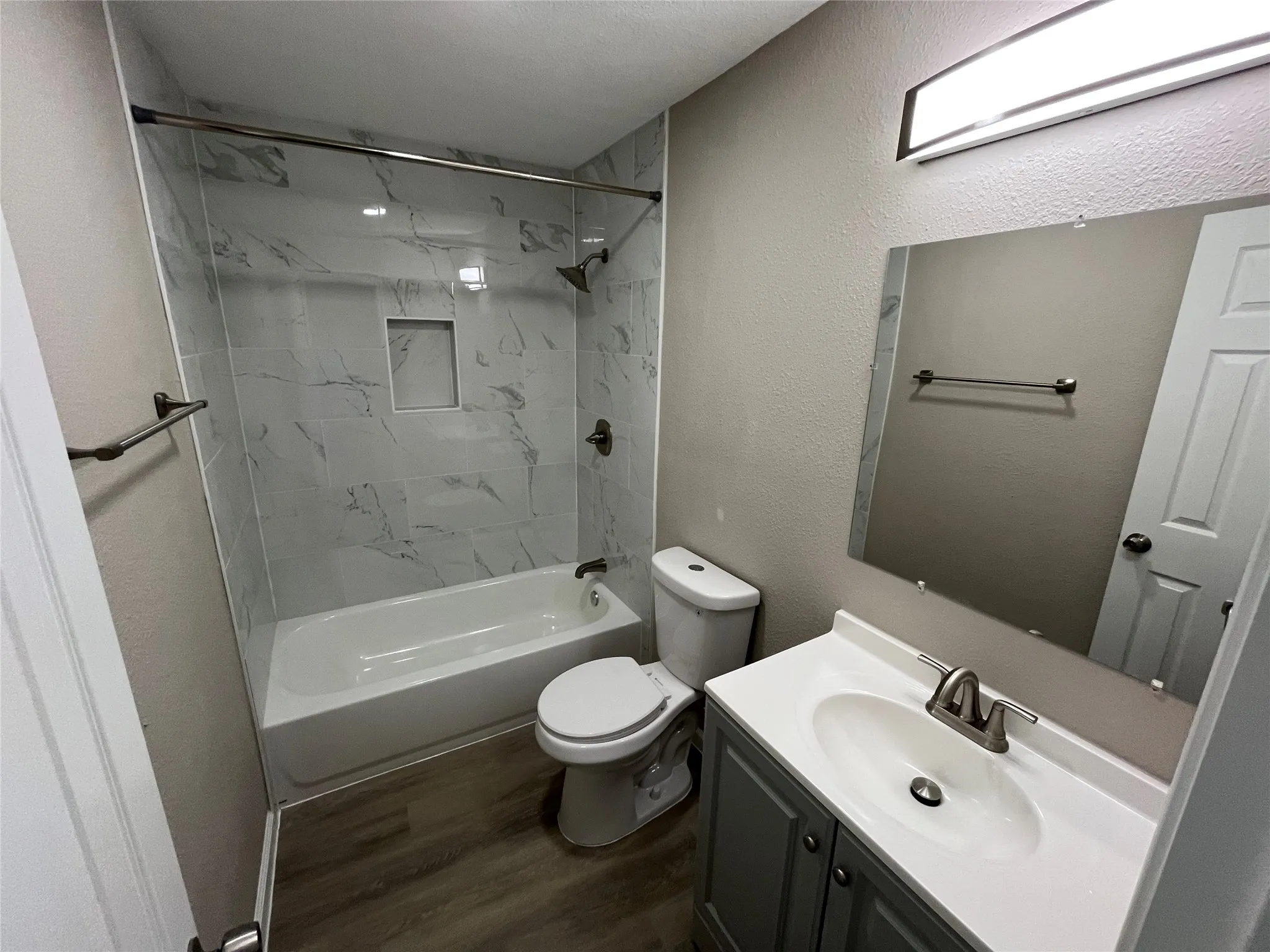 Full bathroom featuring a single vanity with storage, a toilet, and a combined tub and shower with a tile surround and recessed niche