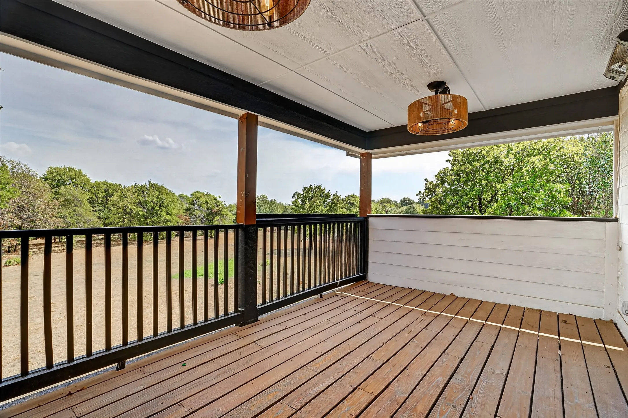 Expansive covered porch featuring wood-finish flooring, black railing, and two decorative ceiling lights