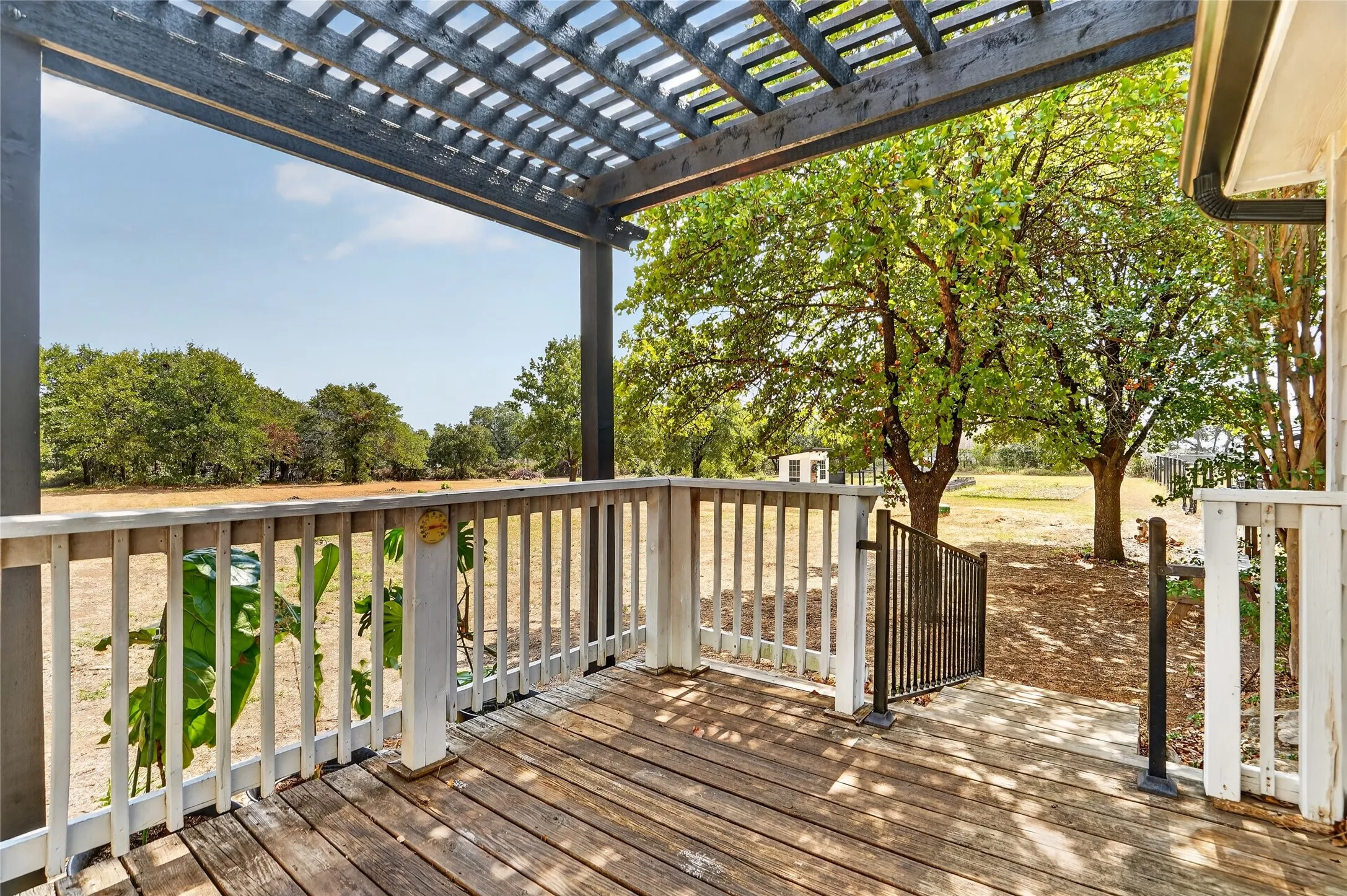 Wood-finish decking with white picket railings, an overhead pergola, and a black metal gate