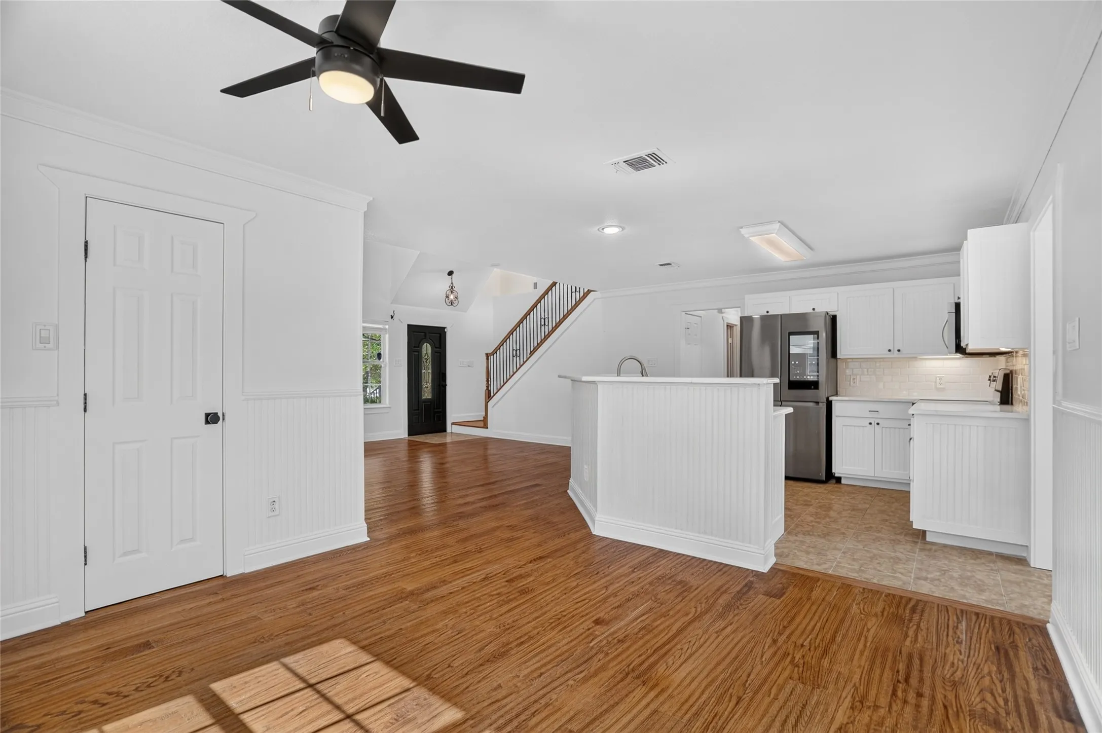 Hardwood-finish flooring, white beadboard paneling, white cabinetry, stainless steel refrigerator, and a ceiling fan with integrated lighting
