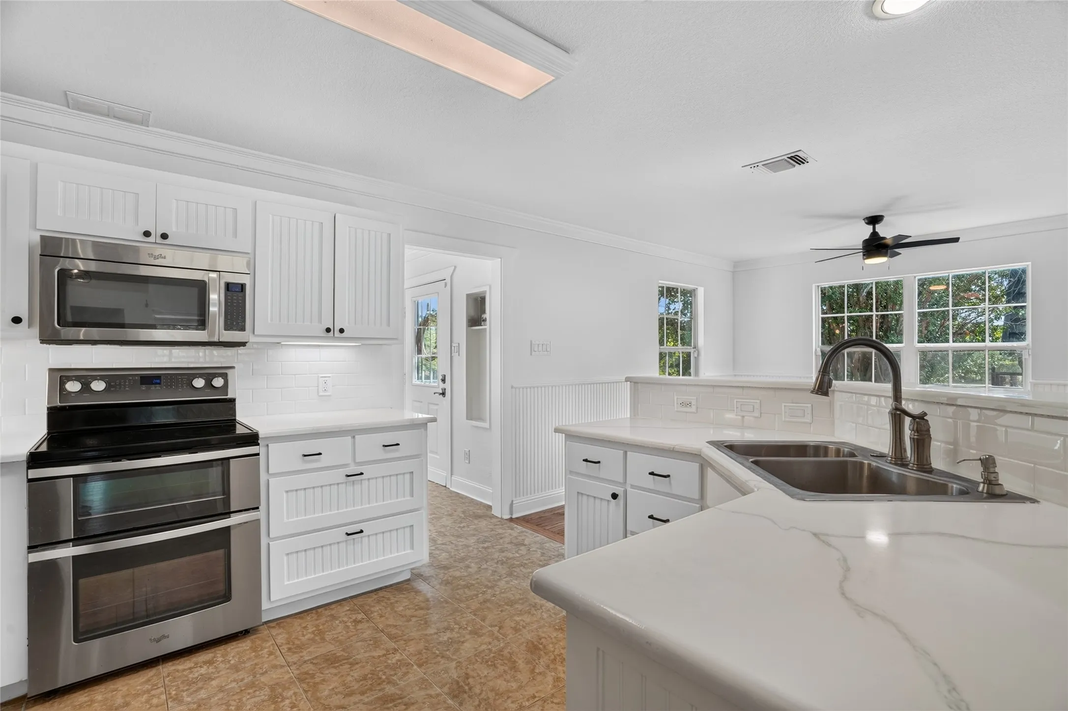 White cabinetry with black hardware, stainless steel appliances, white subway tile backsplash, and light-toned countertops