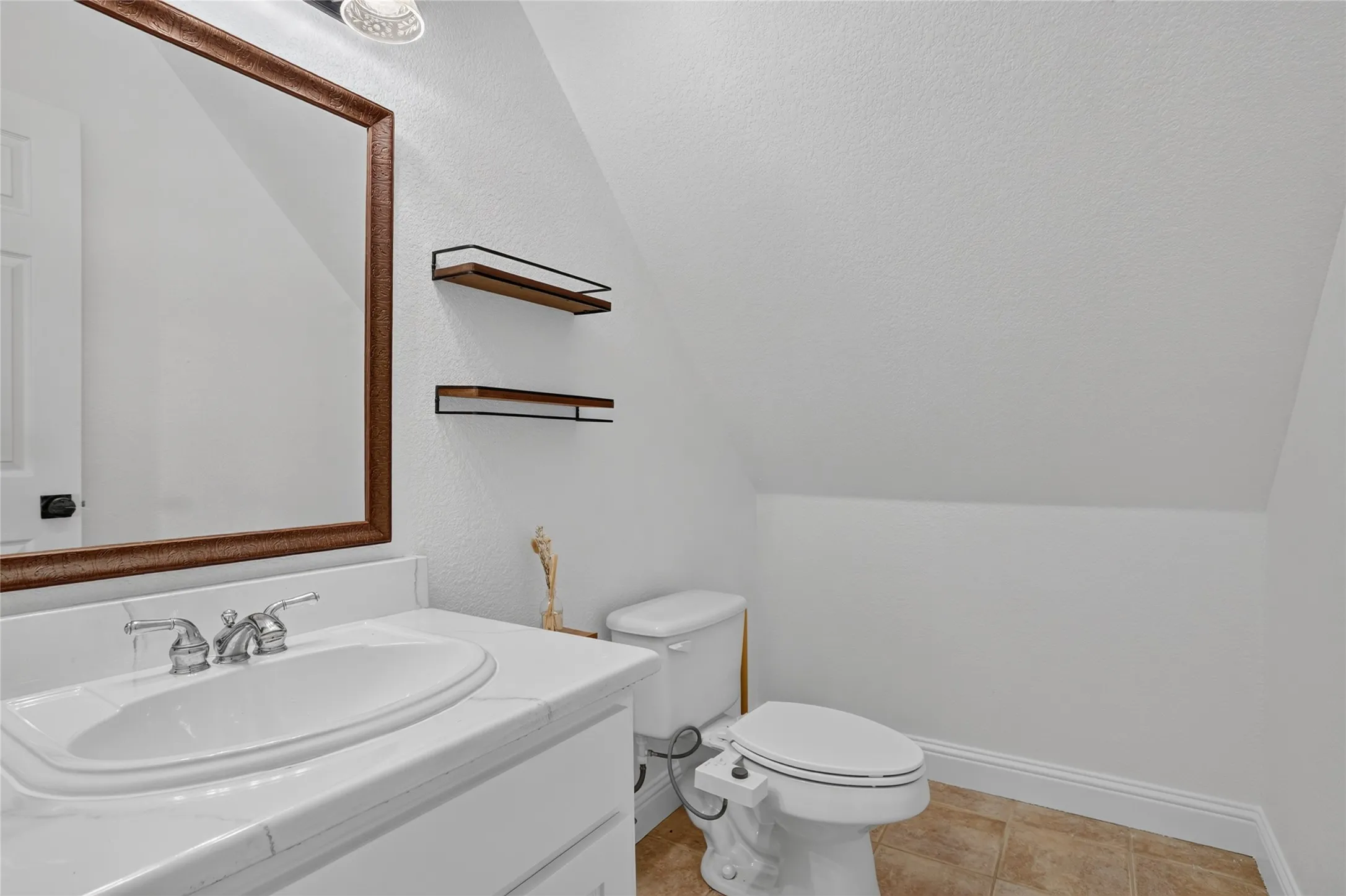 Vanity with an integrated sink, framed mirror, two floating shelves, and tile flooring