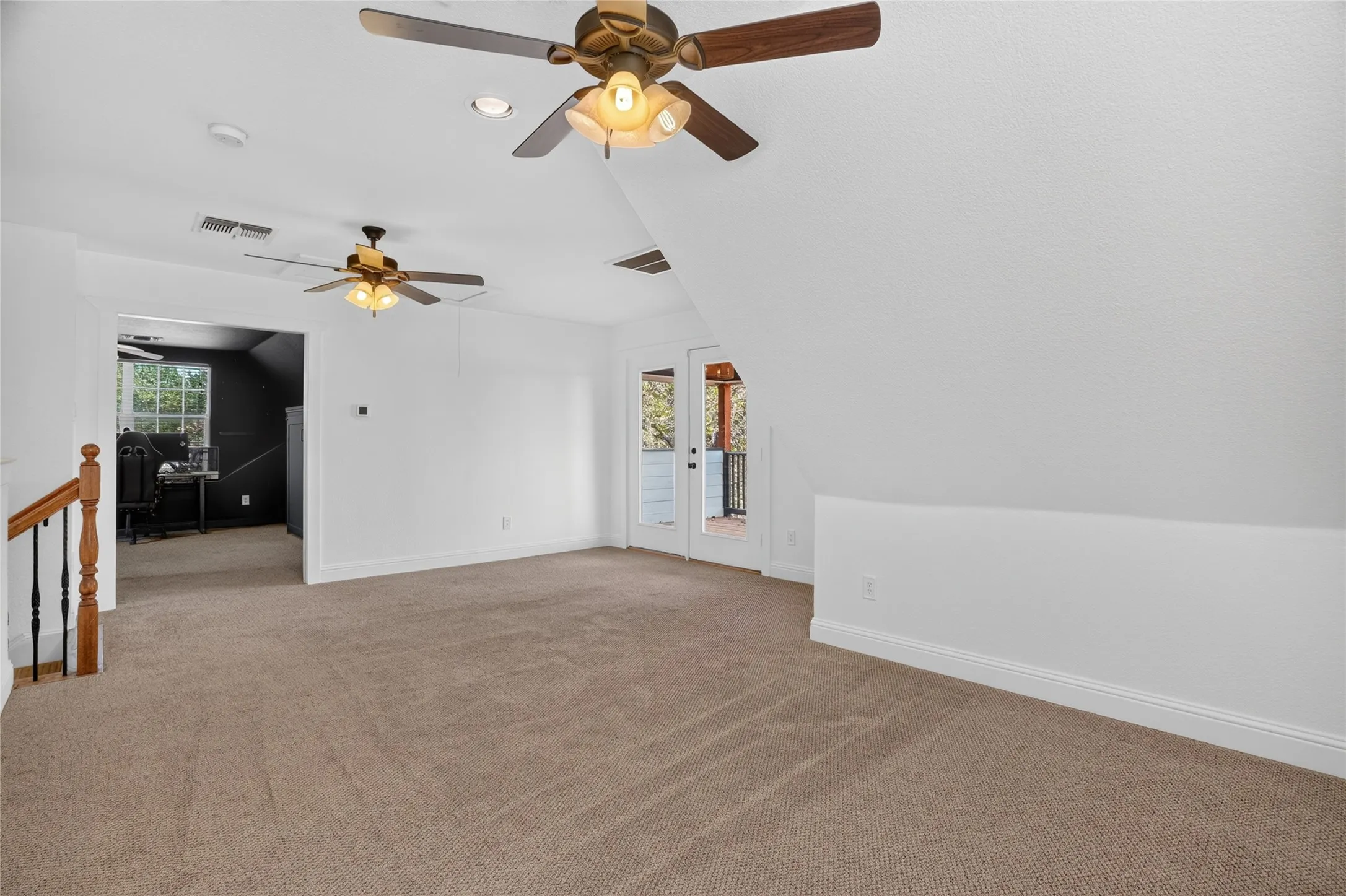 Carpeted floor, multiple ceiling fans with integrated lighting, white walls, and a door leading to an exterior space