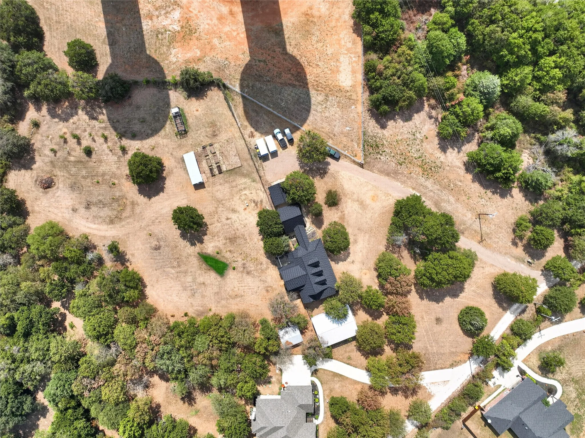Expansive property featuring a residence with a dark roof, surrounded by mature trees, unpaved paths, and open land