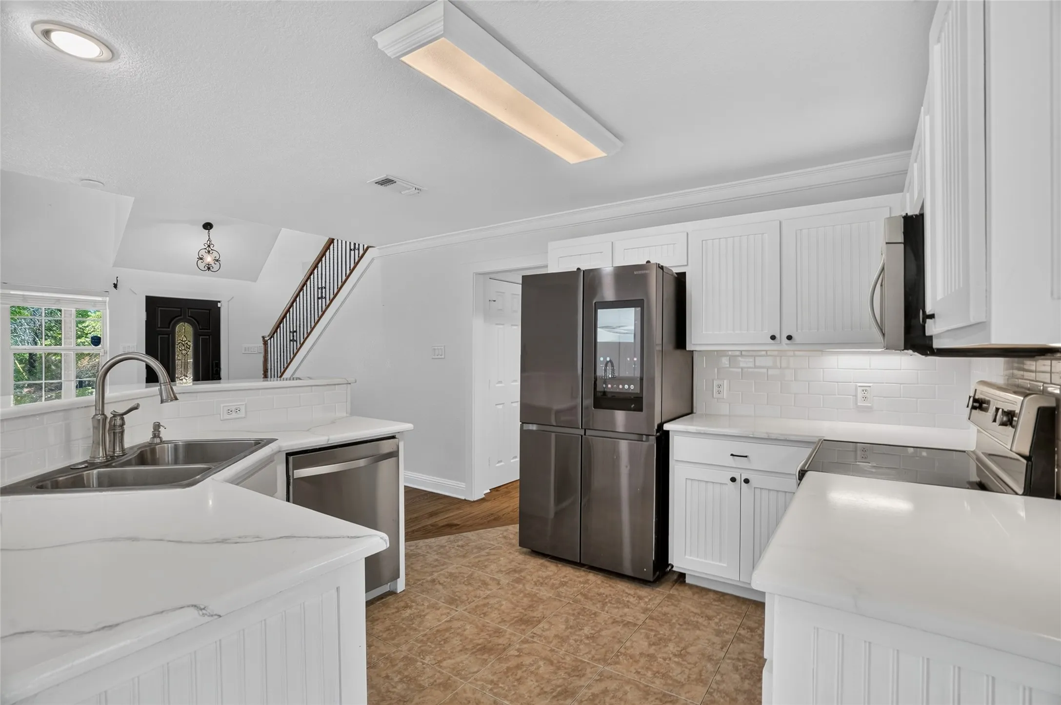 White cabinetry, stainless steel appliances, white subway tile backsplash, and light-toned countertops