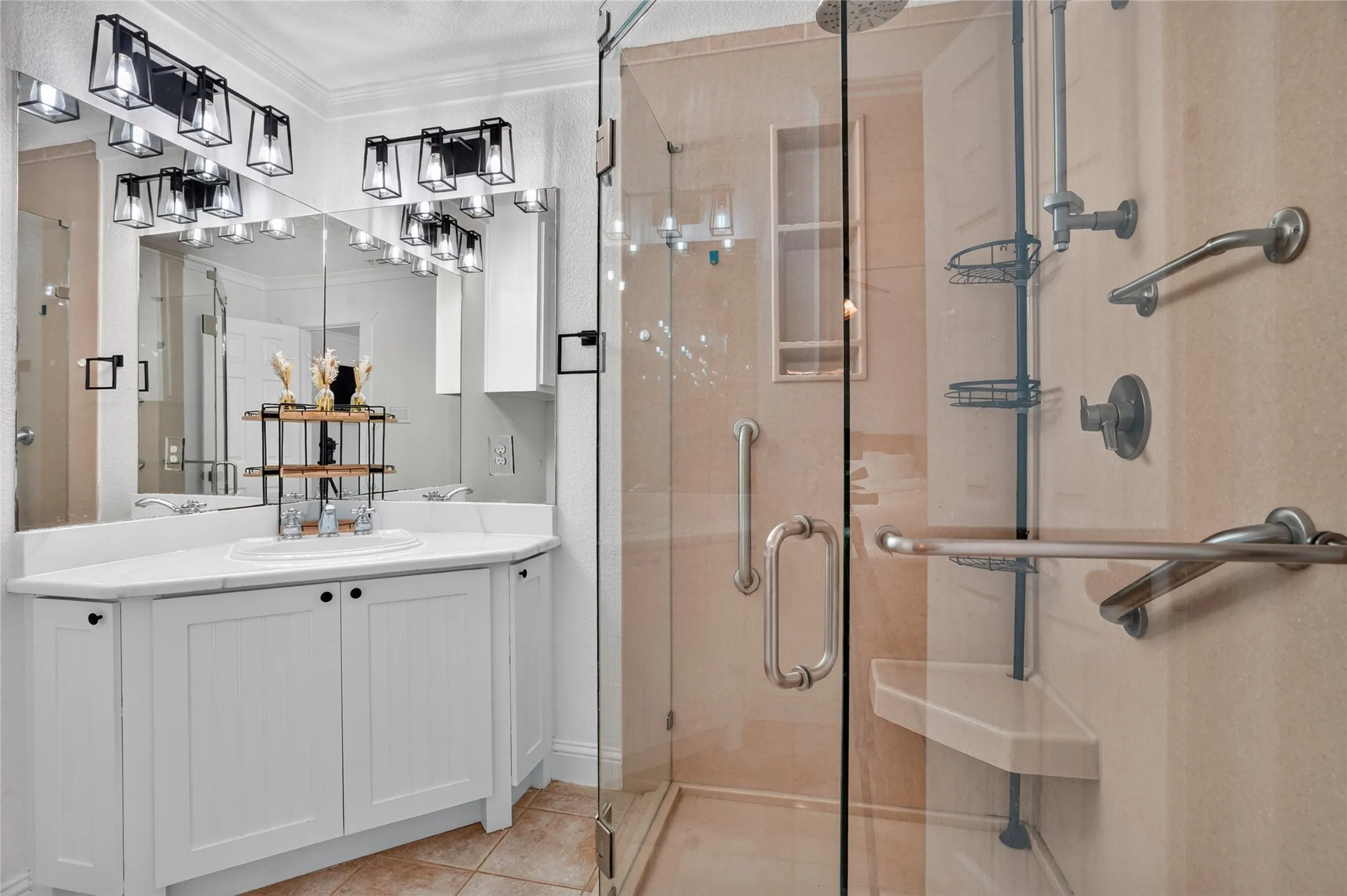 White vanity with integrated sink, glass-enclosed shower, and tile flooring