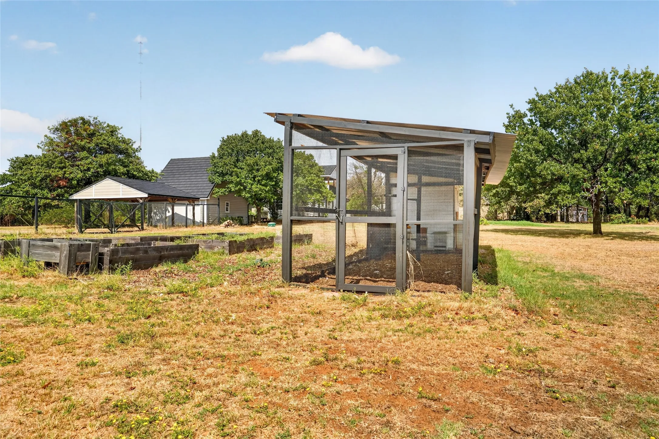 Exterior property featuring a screened enclosure, multiple raised garden beds, and a covered structure