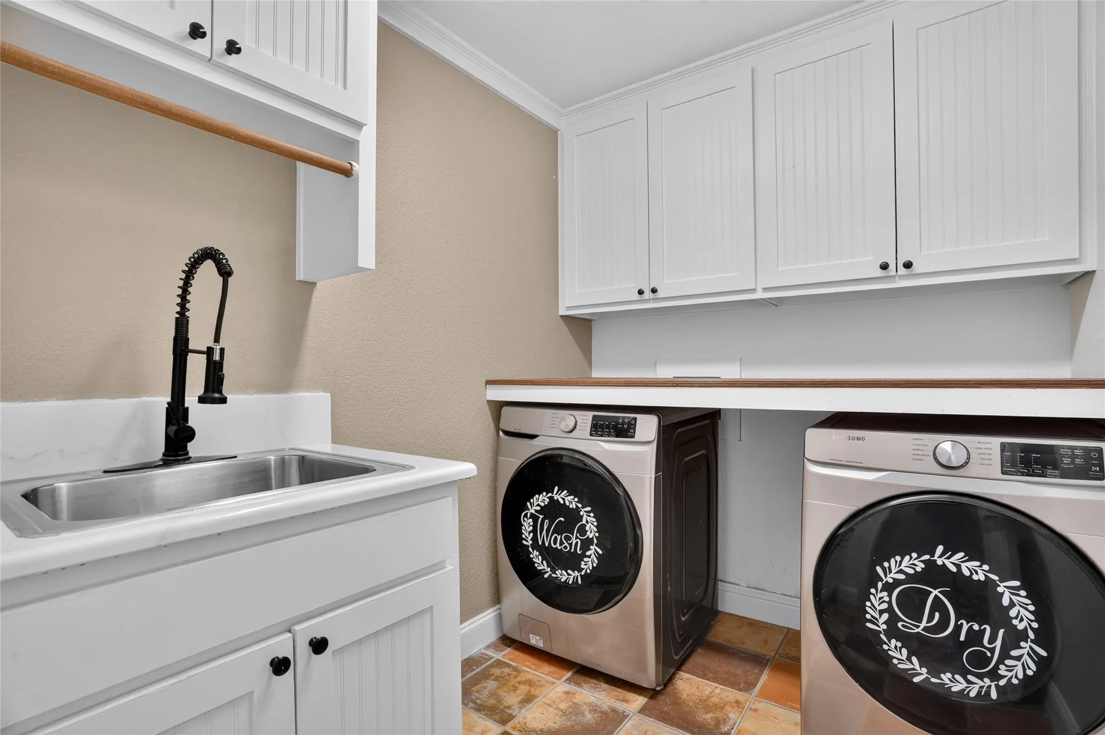 Laundry area featuring white beadboard cabinetry, a stainless steel utility sink with a matte black faucet, and wood-finish countertops