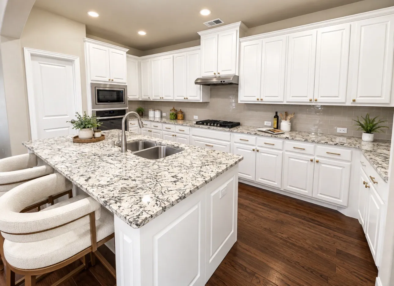 Kitchen featuring dark wood-finish flooring, white cabinetry, integrated stainless steel appliances, a center island with a double basin sink, and light-toned countertops