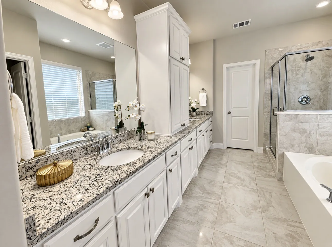 Dual vanity with undermount sinks, stone countertops, white shaker cabinetry, tiled flooring, and a glass-enclosed shower