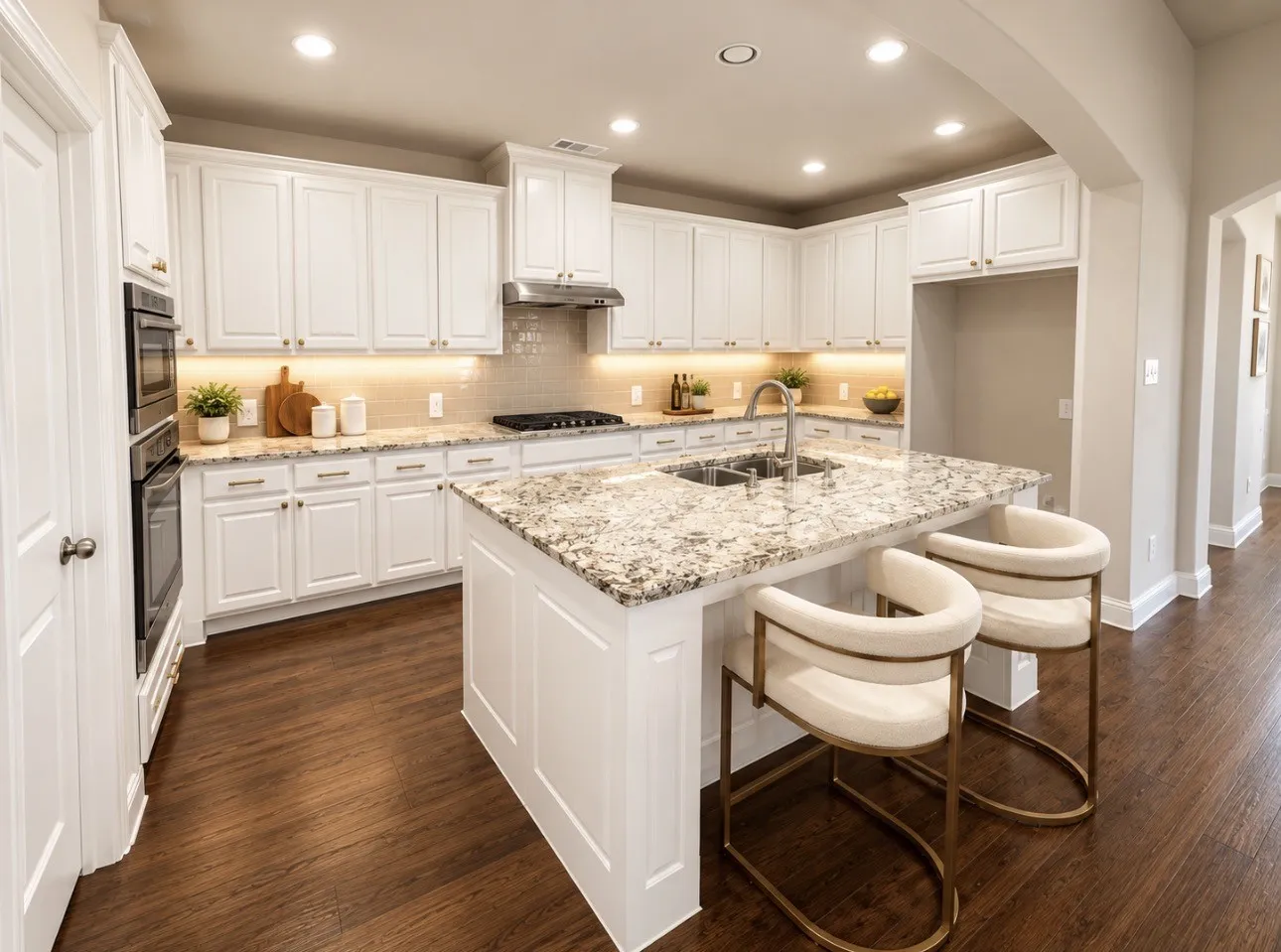 White cabinetry with under-cabinet lighting, stainless steel double ovens, a kitchen island with granite countertop, a double basin sink, and wood-finish flooring